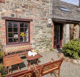 Outside seating area with wooden benches and a table in front of stone wall cottage at Ash Cottage in Warbstow