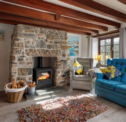 A living room with a stone fireplace wood stove armchair blue sofa and colorful rug at Pond Meadow in Warbstow