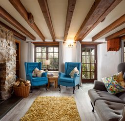 A living room with stone fireplace blue armchairs and a gray sofa at Little Leighs in Warbstow
