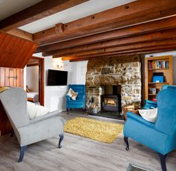 A living room with wooden beams a stone fireplace and upholstered armchairs at Little Leighs in Warbstow