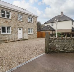 Stone cottage with white door and windows gravel driveway and stone wall with a sign in front at About Time Cottage in Parkend