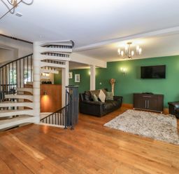 A living room with a white spiral staircase leather sofas wooden floor and a green wall with a TV at About Time Cottage in Parkend