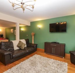 A living room with two black leather sofas a wall-mounted TV a dark wooden cabinet a green wall and a pool table at About Time Cottage in Parkend
