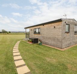 A wooden cabin with a stone path and grass field at Cotswold View 1 in Honeybourne