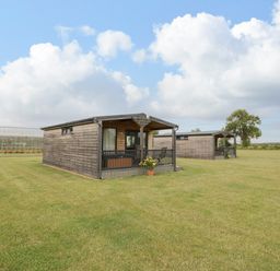 Two wooden cabins on a large grassy field under a cloudy sky at Cotswold View 2 in Honeybourne