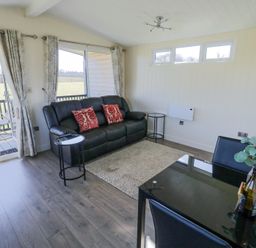 A living room with a black sofa red pillows glass dining table and outdoor view at Cotswold View 2 in Honeybourne