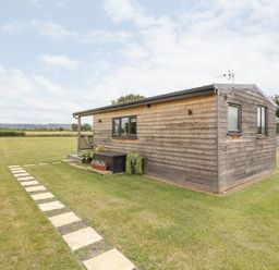 An exterior view of a wooden cabin with a pathway and grassy field at Cotswold View 3 in Bretforton near Evesham