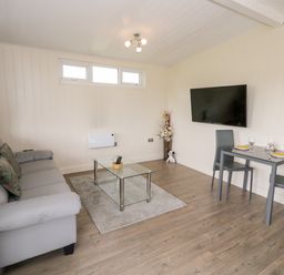 A living room with a grey sofa glass coffee table and a small dining table with two chairs at Cotswold View 3 in Bretforton near Evesham
