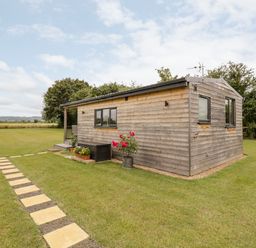 A small wooden cabin with windows and flowers on grass with stone path at Cotswold View 4 Bretforton near Evesham