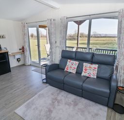 A living room with a gray sofa and sliding glass doors opening to a grassy field at Cotswold View 4 in Bretforton near Evesham
