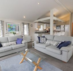 A living room with two gray sofas and a glass coffee table near a kitchen at Oyster Bay Lodge in Dalbeattie