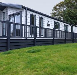An exterior view of a white and black mobile home with a porch and railing on a grassy lawn