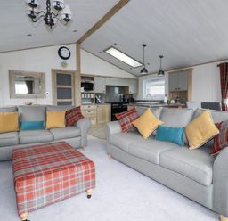 A living area with two grey sofas and a plaid ottoman in front of a kitchen at Beachcliff in Porth