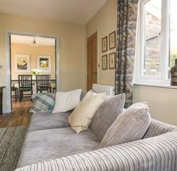 A living room with a gray sofa and pillows next to a window showing a dining area at Crantock Lodge in Crantock