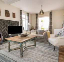 A living room with a wooden coffee table a sofa an armchair a television and a wood-burning stove at Crantock Lodge in Crantock