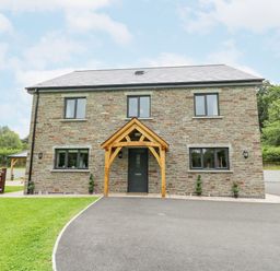 A stone house with wooden porch over the front door and paved driveway at Talarddu Cottage in Builth Wells
