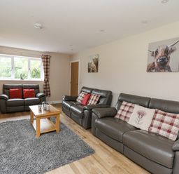A living room with leather sofas wooden coffee table and animal paintings at Talarddu Cottage in Builth Wells