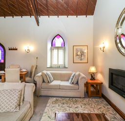 A living room with beige sofas a wooden coffee table a patterned rug wall lamps and a stained glass window at Frogwell Chapel in Frogwell near Callington