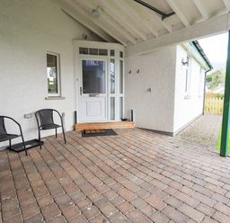 A covered patio with two black chairs and a white door at Limhus Cottage in Keswick
