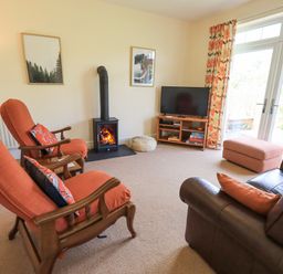 A living room with orange armchairs a leather sofa a wood stove and a television at Limhus Cottage in Keswick