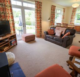 A living room with a leather sofa orange armchairs a TV on a wooden stand and a dining table with chairs at Limhus Cottage Keswick