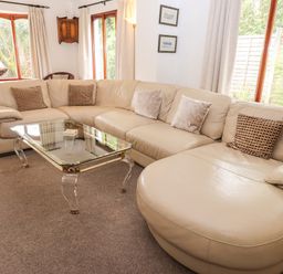 A living room with a large beige sectional sofa and a glass coffee table at Fir Trees in Bowness-On-Windermere