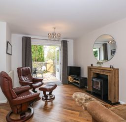 A living room with two brown leather chairs a small wooden mantel with a round mirror above a fireplace and a TV unit near a door leading to a patio at The Sanctuary in Windermere