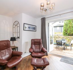 A sitting area with two brown leather chairs a table with a lamp a wall mirror and an open door leading to a patio with a table and chairs at The Sanctuary in Windermere