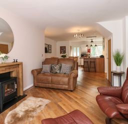 An open plan living room and kitchen with brown leather sofa and chairs wooden floor and a small fireplace at The Sanctuary in Windermere