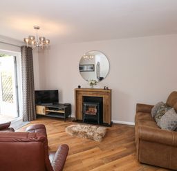 A living room with brown leather chairs a brown sofa a wooden floor a small fireplace a round mirror above the fireplace and a TV on a stand at The Sanctuary in Windermere