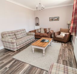 A living room with sofas a coffee table a rug and framed pictures on the wall at Deanrise in Shilbottle near Alnwick