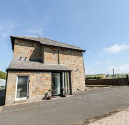 A stone house with a slate roof on a paved area with a gated fence and countryside beyond at Deanrise in Shilbottle near Alnwick