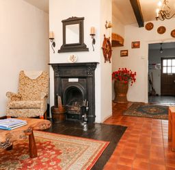 A room with a floral armchair a wooden coffee table books a fireplace a mirror wall sconces a hallway with a rug and a wooden door at Harbour Cottage in Watchet