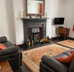 A living room with a black fireplace a mirror above it two sofas a television on a wooden stand and an orange patterned rug at Harbour Cottage in Watchet