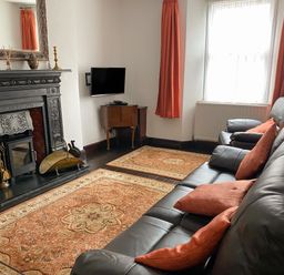 A living room with a black fireplace a wall mounted TV leather sofas orange cushions and curtains at Harbour Cottage in Watchet