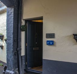 An open black door on a building with cream and black walls and small potted plants on the exterior wall at Ferrystone in Kingswear near Dartmouth