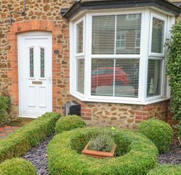 Front door and bay window of a house with brick and stone exterior and manicured bushes in garden at Hunny Cottage in Hunstanton