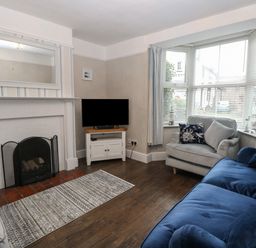 A living room with a fireplace tv on a stand two sofas and a window with blinds and curtains at Hunny Cottage in Hunstanton