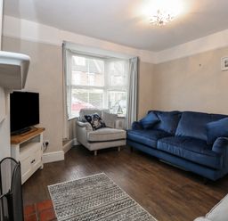 A living room with a blue sofa a grey armchair a television on a stand and a fireplace at Hunny Cottage in Hunstanton