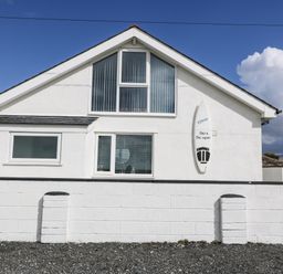 The front exterior of a white house with multiple windows and a surfboard mounted on the wall at Sea Scape in Dinas Dinlle