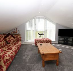 A living room with patterned sofas a wooden coffee table a television on a stand and a telescope near a window at Sea Scape in Dinas Dinlle
