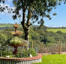 A garden with a three-tier flower planter and a tree overlooking fields and hills at Woodhall in Cardinham