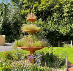A tiered garden planter with plants and flowers in a fenced flower bed with trees and a wooden gate in the background at Woodhall in Cardinham