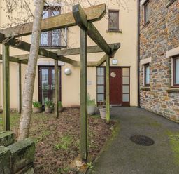 An outdoor area with wooden pergola plants in pots and a pathway leading to brown doors at 2 Chandlers Yard Burry Port