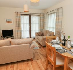 A living room with two beige sofas and a wooden dining table set for four at 2 Chandlers Yard in Burry Port