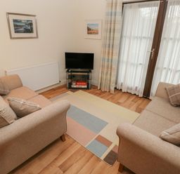 A living room with two beige sofas cushions a small television on glass stand and a patterned rug at 2 Chandlers Yard in Burry Port