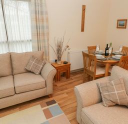 A living room with two beige sofas, a small wooden table with a vase, and a dining table set for four at 2 Chandlers Yard in Burry Port
