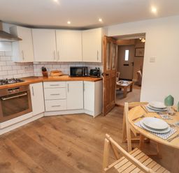 A kitchen with white cabinets wooden countertops and a dining table set for two at The Cottage in Tetbury