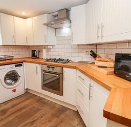 A kitchen with white cabinets wooden countertops a washing machine oven microwave and bread on a cutting board at The Cottage in Tetbury