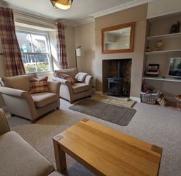 A living room with armchairs a wood stove a television and bookshelves at The Cottage in Tetbury